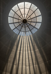 Naklejka premium A decorative domed ceiling with prominent skylight is part of the interior architecture of Modern building. its iris diaphragm-like pattern and the way sunlight streams through it, creating visible ra