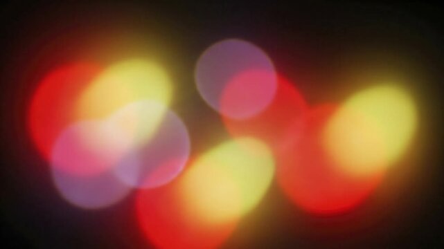Soft vibrant blurred light circles and ovals in red yellow and pink hues create an abstract pattern on a dark background
