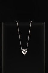 A heart shaped diamond pendant with a chain is displayed in a black box