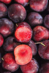 Fresh Red Plums Pile with Cut Halves Showing Juicy Interior