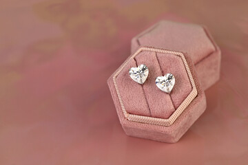 A pair of diamond earrings are displayed in a pink velvet box