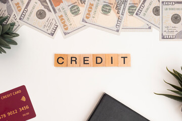 Wooden block tiles with the letters "Credit" on a white background. The word "Credit" is written on a wooden block or wooden cube with money, books, and credit cards on an office desk.