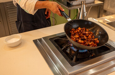 A chef is cooking food in a pan on a stove. The pan is filled with meat and vegetables