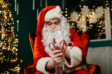 Santa claus holding candy canes near decorated christmas tree