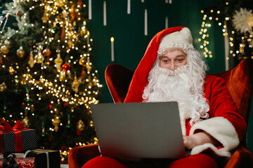 Santa claus using laptop near christmas tree