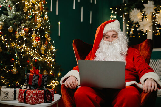 Santa claus using laptop near christmas tree and gifts