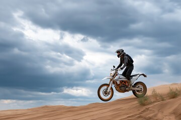 Obraz premium Male riding motorcycle across desert sand dunes under cloudy sky adventure