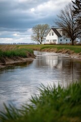 Fototapeta premium Peaceful rural landscape with stream and white farmhouse under cloudy sky