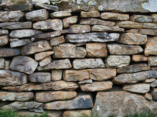 Stacked stones of a rustic dry stone wall close up - A detailed close-up of a traditional dry stone wall, showing the texture, colors, and natural patterns of the stacked rocks.
