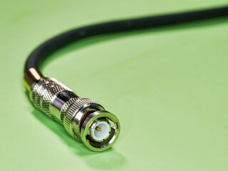 BNC connector at the end of a black cable - A detailed close-up of a shiny BNC connector attached to a black coaxial cable, isolated on a green background.