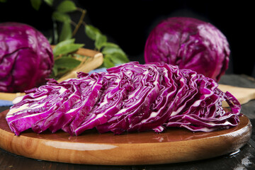 Obraz premium Fresh Purple Cabbage Sliced on Wooden Cutting Board with Leafy Green Vegetables
