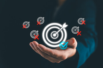 Hand of businessman focusing on one main target with glowing dartboard and check mark, symbolizing concentration, clarity, and success in achieving a single important business goal.