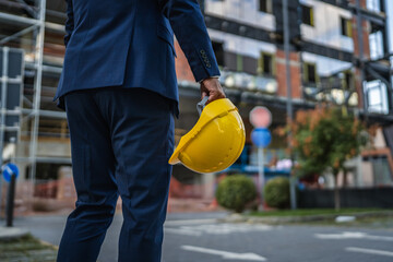 Architect holding yellow helmet visiting construction site
