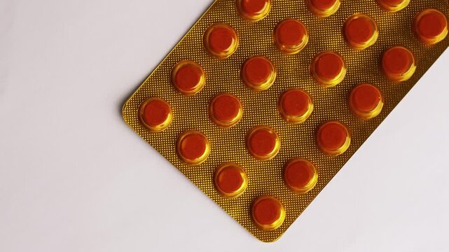 Golden blister pack filled with round brown pharmaceutical tuberculosis pills arranged in uniform rows on a clean white background surface