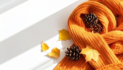 Autumnal background with a yellow knitted scarf, orange leaves and pine cones in sunlight. 