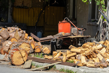 A robust log splitter sits amidst large piles of freshly cut and split firewood outside a house, ready for winter heating. The scene conveys a sense of rural work and preparation.