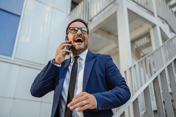 Businessman laughing while talking on phone outside office building