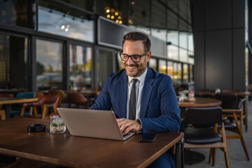 Happy businessman smiling at outdoor cafe with laptop