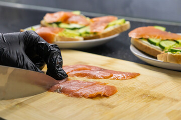 Professional chef's gloved hand expertly slicing fresh smoked salmon fillets on a rustic wooden...