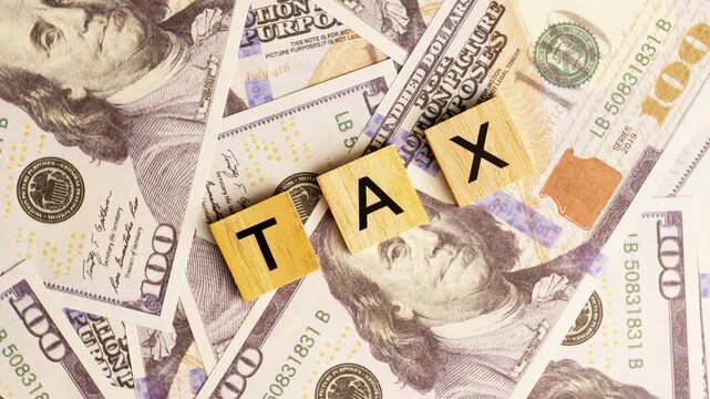 Wooden blocks with the letters "Tax" arranged on a slowly rotating stack of dollar bills. Looping 360-degree of wooden blocks with the words "Tax" as a business financial concept. 4K footage.