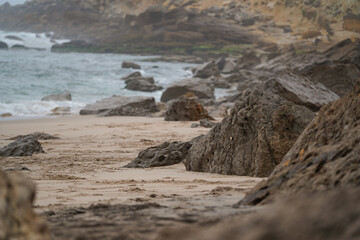 Rocky coast at Praia Pequena do Rodízio, Sintra, Portugal. Waves, stratified cliffs, sand, and clouds. Natural erosion, geological structure, coastal landscape.