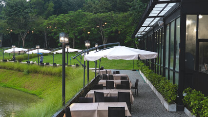 Contemporary outdoor lounge area with sofas and white umbrellas, located in a lush garden setting with path lighting.