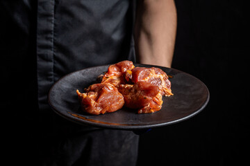 Raw marinated meat pieces on a black plate