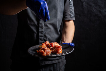 Chef sprinkling salt on raw marinated pork