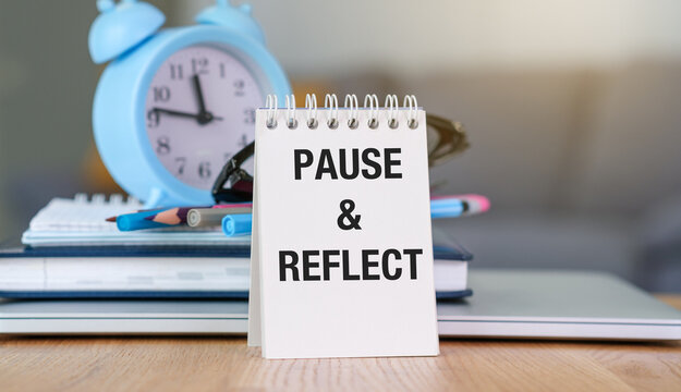 Pause and reflect. Words on a notebook , white background with alarm clock