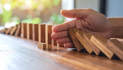 Hand stopping dominoes from falling, preventing chain reaction.