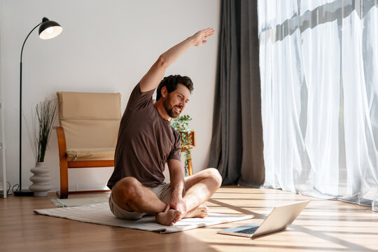 Man Doing Online Yoga Class at Home Stretching on Floor