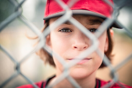 Young boy play baseball on summer day through fence - Powered by Adobe