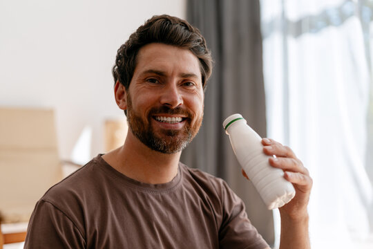 Smiling man drinking yogurt at home