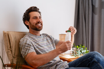 Happy man opening bottle of yogurt drink sitting on armchair at home