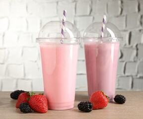 Tasty milkshakes in plastic cups and fresh berries on wooden table, closeup