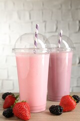 Tasty milkshakes in plastic cups and fresh berries on wooden table, closeup