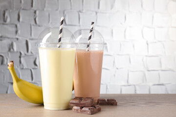 Tasty milkshakes in plastic cups and ingredients on wooden table, closeup. Space for text