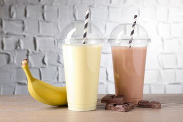 Tasty milkshakes in plastic cups and ingredients on wooden table, closeup