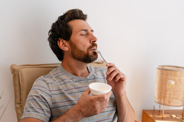 Man enjoying yogurt on armchair at home