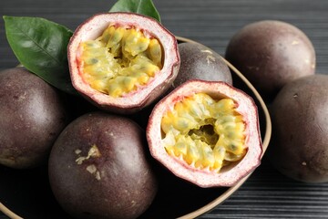 Fresh passion fruits with green leaves on black wooden table, closeup
