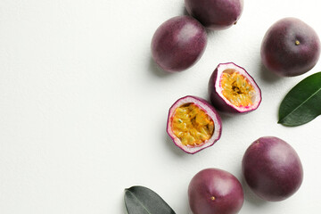 Fresh passion fruits with green leaves on white table, flat lay. Space for text