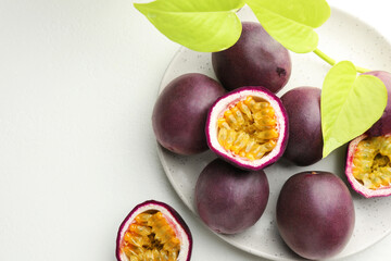 Fresh passion fruits with green leaves on white table, above view. Space for text