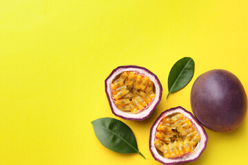 Fresh passion fruits with green leaves on yellow background, flat lay. Space for text