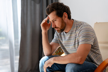 Worried man suffering from headache sitting on chair at home