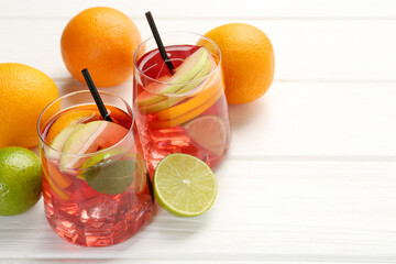 Tasty punch with ice, mint and slices of fruits in glasses on white wooden table, closeup with space for text. Refreshing drink
