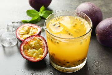 Tasty passion fruit drink with mint, ice cubes and fresh fruits on grey table, closeup