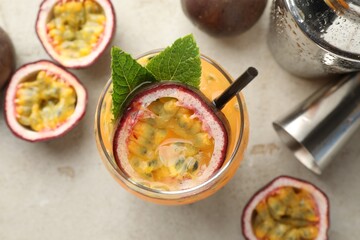 Tasty passion fruit drink with mint in glass, fresh fruits, shaker and jigger on gray table, flat lay