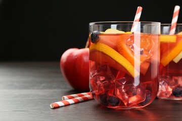 Tasty punch in glasses and fresh fruit on wooden table against black background, closeup. Refreshing drink