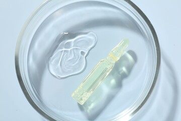 Glass ampoule with cosmetic product and Petri dish on light blue background, top view