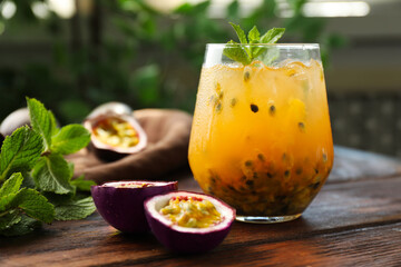 Tasty passion fruit drink with mint in glass and fresh fruits on wooden table, closeup